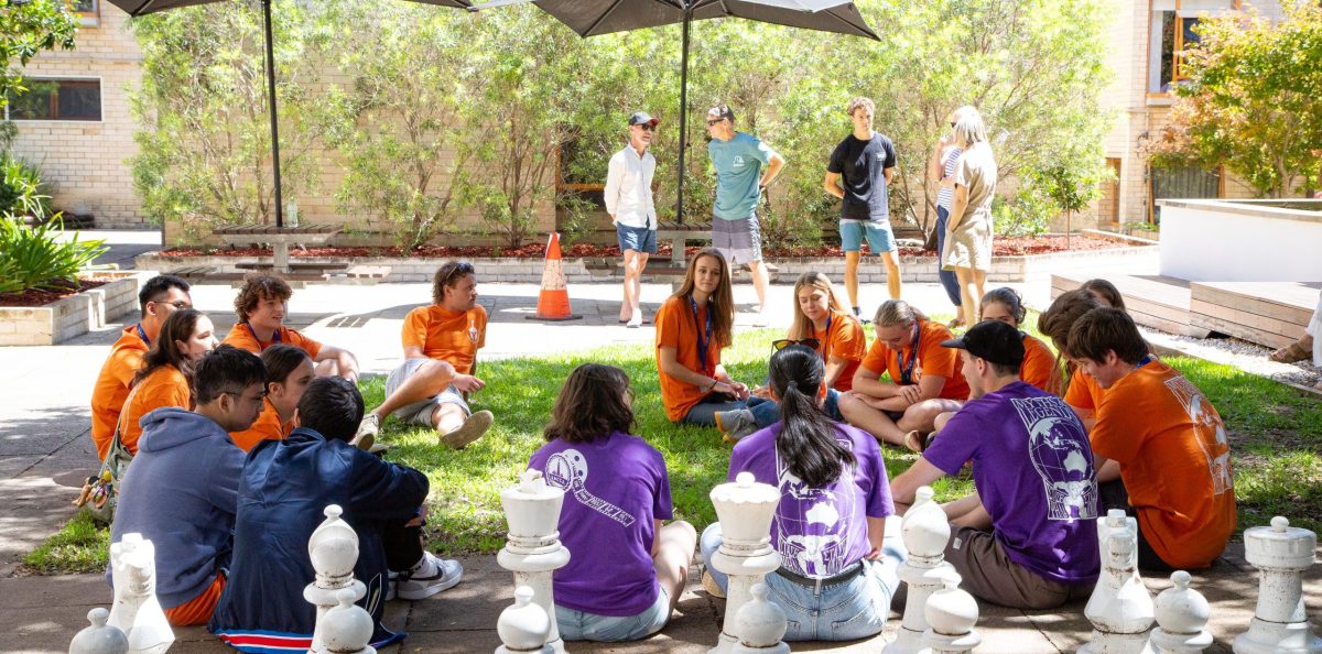New residents sitting in a circle on the courtyard lawn with student leaders in purple shirts at Robert Menzies College.